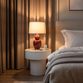 Bedroom with a nightstand featuring a lamp and small items, next to a bed with gray bedding.