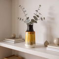 Vase with eucalyptus on a shelf against a plain wall