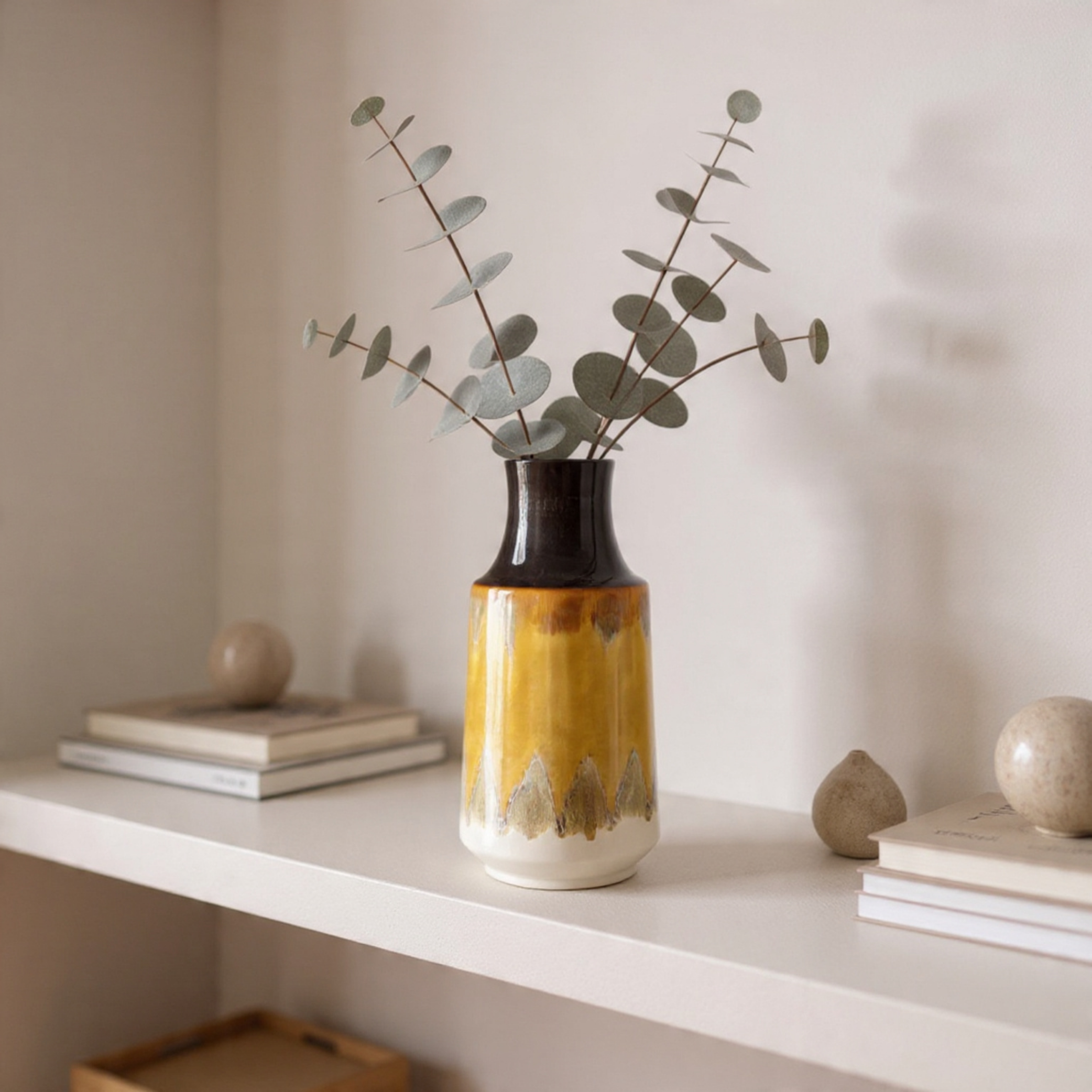 Vase with eucalyptus on a shelf against a plain wall