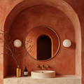 Bathroom with terracotta walls, round mirror, and stone sink.