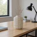 Decorative vase on a wooden desk with a lamp and books in the background