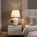 White lamp on a nightstand next to a bed with gray bedding.