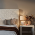 Cozy bedroom with textured headboard, nightstand with lamp and candles, and decorative vase.