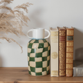 Decorative vase with a checkered pattern on a shelf with books and dried plants.
