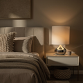 Cozy bedroom with a bed and nightstand featuring a lamp and mug.